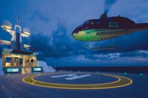 Helicopter approaching a superyacht helideck at dusk, with illuminated yellow circle and white “H” helicopter pad lights integrated into the deck.