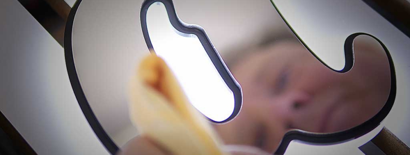 Close-up of a person cleaning a backlit metal yacht emblem or sign, polishing the illuminated surface with a cloth.