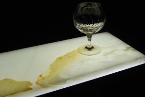 Crystal wine glass on an illuminated marble slab with warm backlighting highlighting natural stone veining against a dark background.