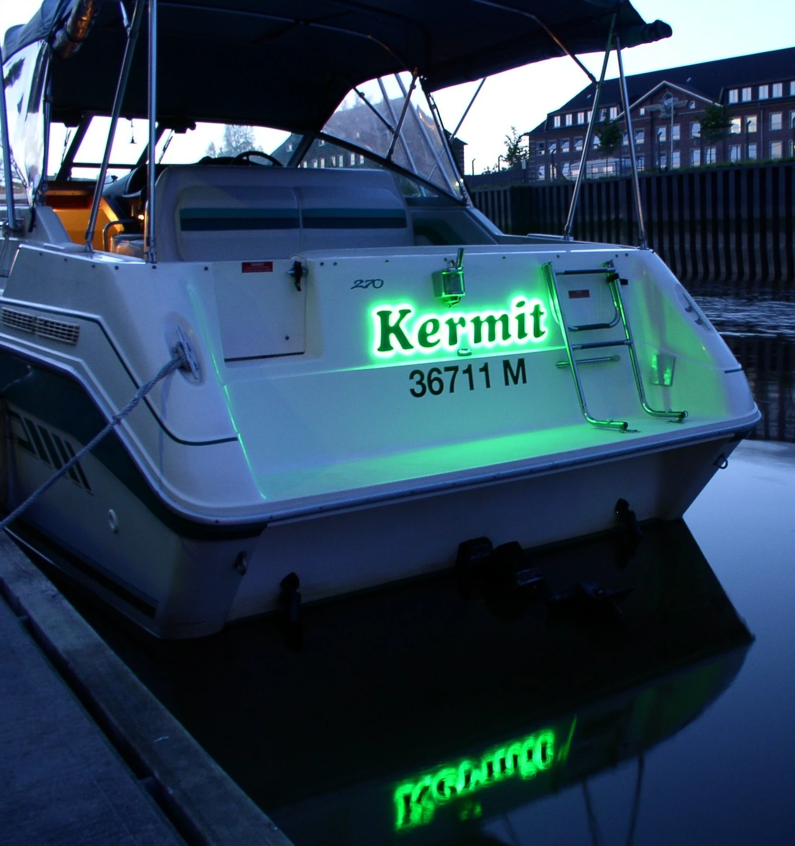 Kermit motorboat moored at a marina at dusk, featuring Yachtlite's first illuminated yacht signs glowing green on the stern
