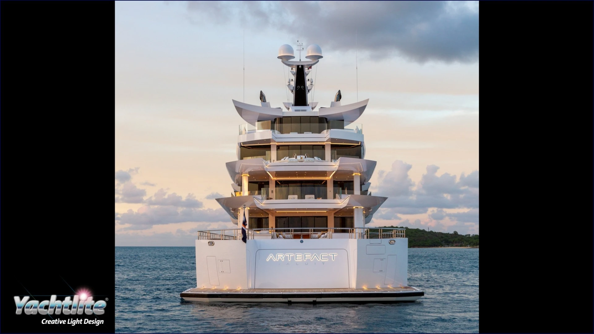 The stern of a large white superyacht in daylight, with warm, gold ambient lighting.