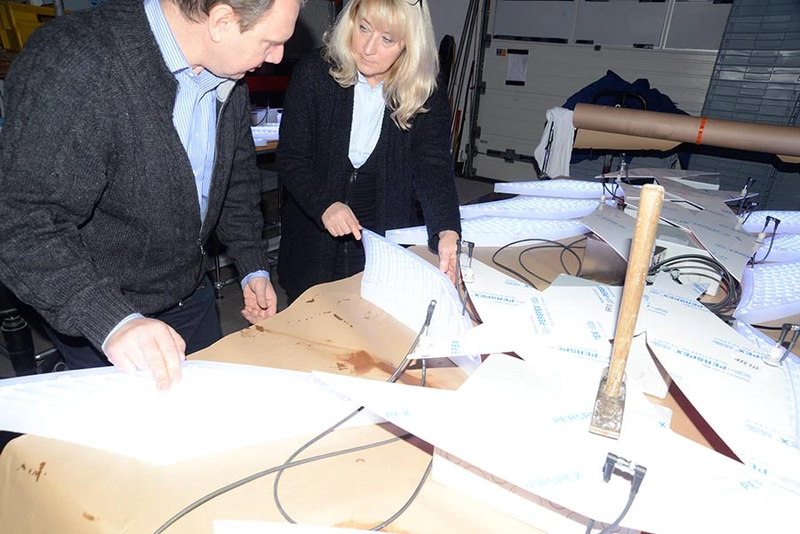 Two designers assemble and inspect illuminated LED sign panels during fabrication in a workshop.