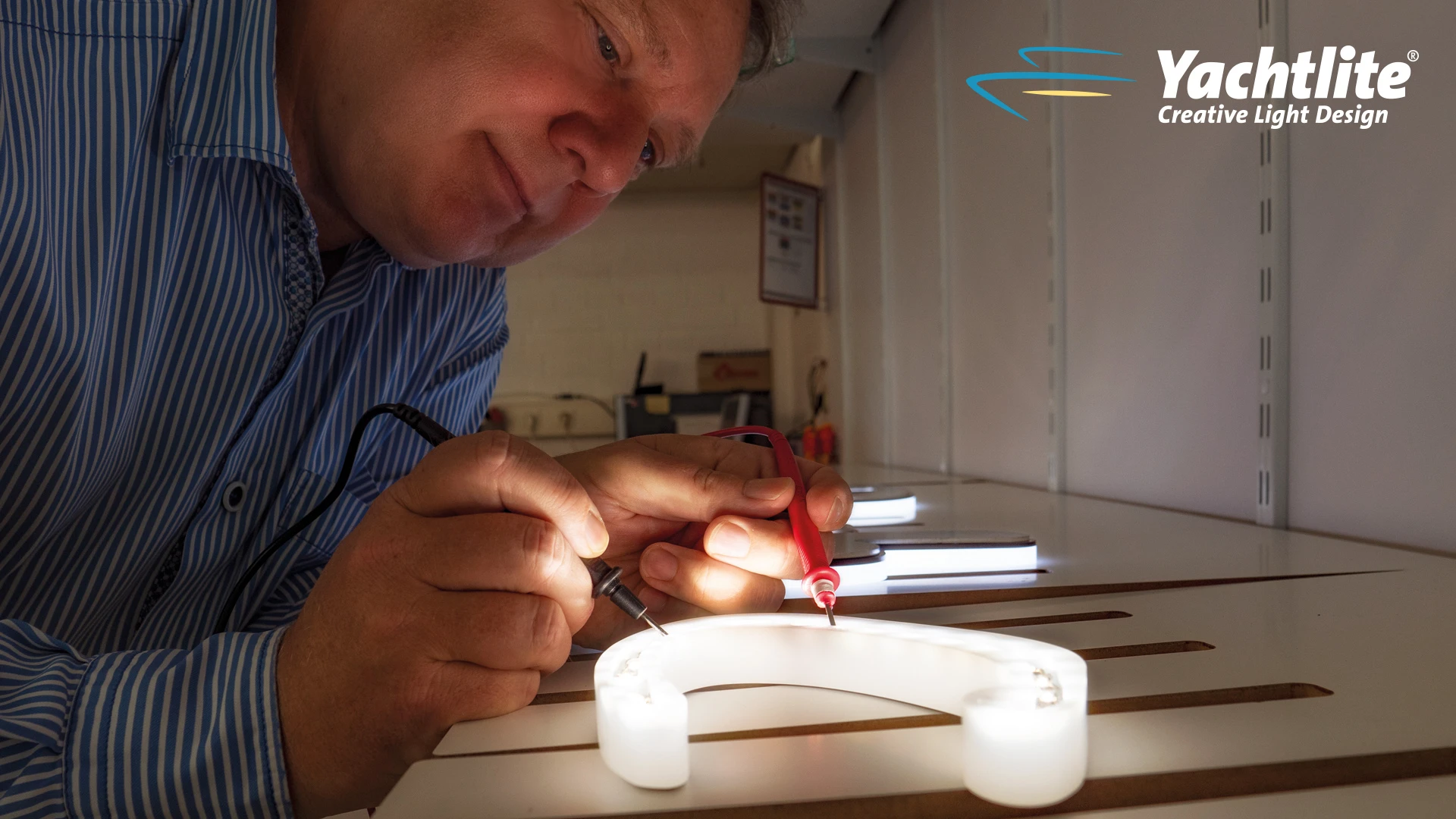 A craftsman testing the illumination and electrical connections of a custom yacht sign during the manufacturing process, with illuminated lettering components on the workbench.