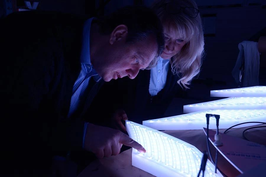 Two designers inspect illuminated LED sign components, testing light quality and craftsmanship during production.